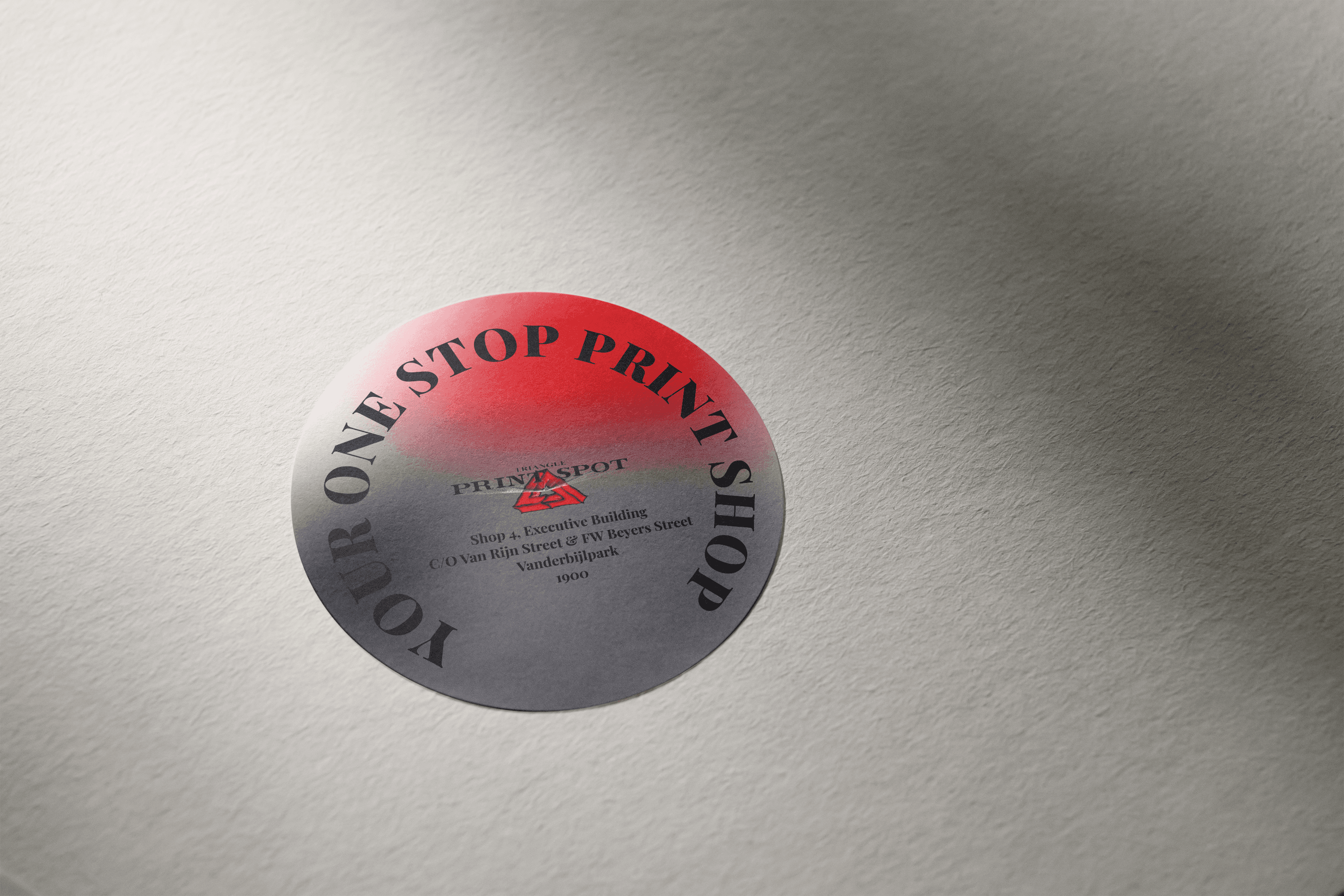 A sticker with red, white, grey and black mesh gradient background with the Triangle Print Spot logo on a white paper, featuring their address and the words, 'Your One Stop Print Shop'